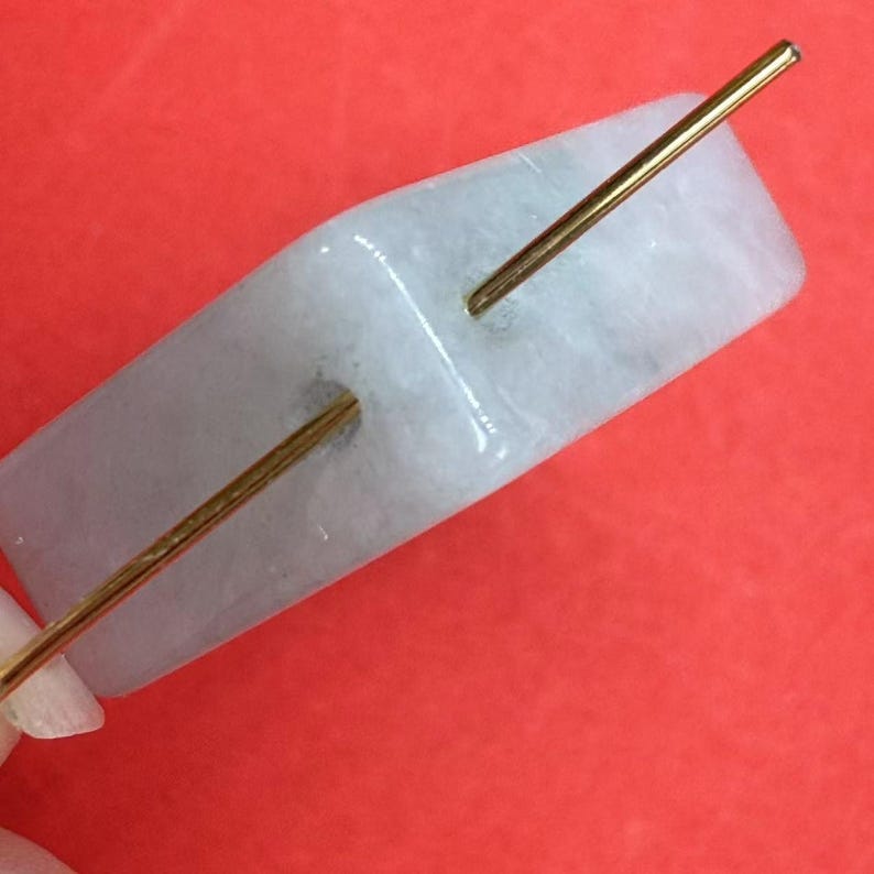 May include: A light blue, rectangular, smooth stone with two holes drilled through it. A gold wire is threaded through the holes.