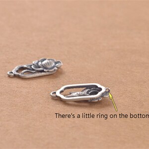 May include: Two silver-toned metal charms shaped like a flower. The charm on the left has a more detailed design with a flower and leaves. The charm on the right has a simpler design with a flower and a small ring on the bottom.