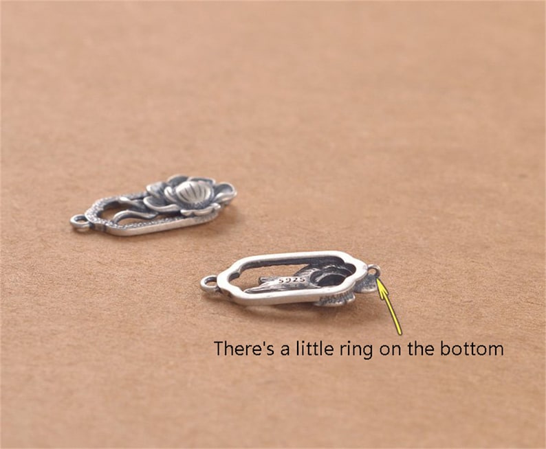 May include: Two silver-toned metal charms shaped like a flower. The charm on the left has a more detailed design with a flower and leaves. The charm on the right has a simpler design with a flower and a small ring on the bottom.