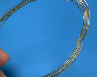 May include: A close-up of a bundle of gold-colored wire, coiled into a circle. The wire is thin and appears to be made of metal.