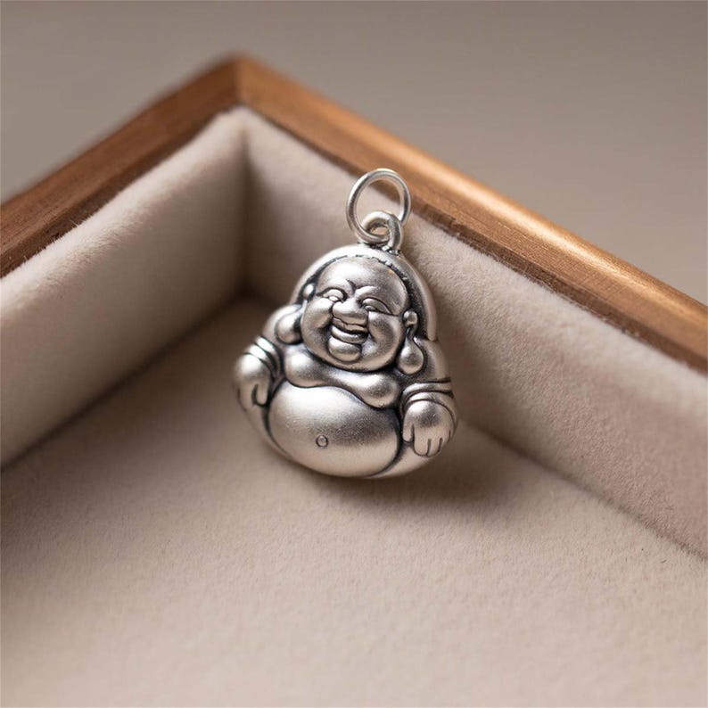 Pu&ograve; includere: Ciondolo in argento a forma di pendente che rappresenta un Buddha sorridente con il viso rotondo e la pancia grande. Il ciondolo &egrave; dettagliato con una superficie testurizzata e un anello per attaccarlo a una collana o un braccialetto.