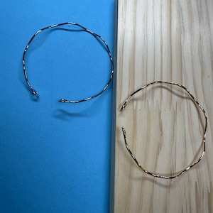 May include: Two simple, minimalist bracelets. One is silver and the other is gold. Both are made of thin, wavy metal.
