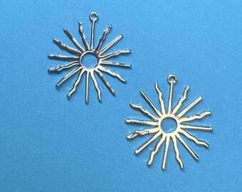 May include: Two silver sunburst charms with a hole at the top for hanging. The sunbursts have a circular center and 16 rays extending outward.