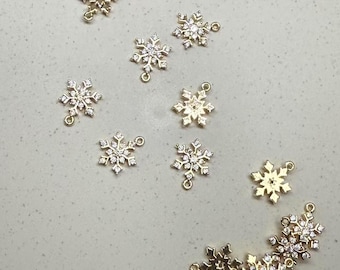 Könnte beinhalten: Eine Sammlung von goldenen Schneeflocken-Anhängern mit klaren Kristall-Akzenten. Jeder Anhänger hat eine Öse zum Anbringen an Schmuck oder andere Bastelarbeiten.