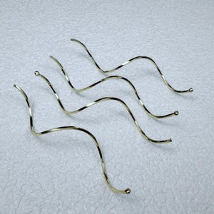 Può includere: Quattro accessori per capelli in metallo ondulato color oro. Ogni pezzo ha un design attorcigliato e una piccola sfera a un'estremità. L'altra estremità ha un piccolo anello. Questi sono probabilmente usati per lo styling decorativo dei capelli.