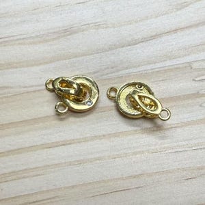 Puede incluir: Dos cierres de metal dorado con un pequeño acento de cristal transparente. Los cierres son redondos y tienen un diseño decorativo.