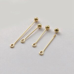 Peut inclure: Plusieurs appr&ecirc;ts de bijoux dor&eacute;s, dont des &eacute;pingles droites avec une petite boucle &agrave; une extr&eacute;mit&eacute; et une perle sph&eacute;rique &agrave; l'autre. Une &eacute;pingle a une extr&eacute;mit&eacute; filet&eacute;e. Les appr&ecirc;ts sont dispos&eacute;s sur une surface de couleur claire.