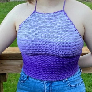 May include: A purple and white ombre crochet halter top. The top is made with a simple stitch and has a relaxed fit.