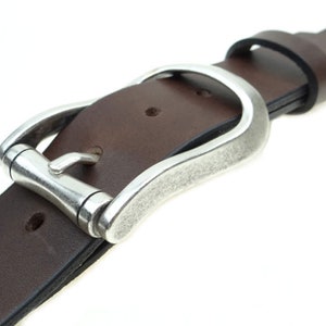 以下が含まれることがあります： 銀色のバックルが付いた茶色の革ベルト。バックルは、湾曲した形状とテクスチャ加工された仕上げで、ユニークなデザインです。