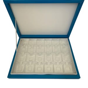 Peut inclure: Boîte d'exposition de bijoux rectangulaire ouverte, avec un extérieur bleu sarcelle et un intérieur blanc. La boîte a un couvercle à charnière et un insert en plastique transparent avec plusieurs compartiments.