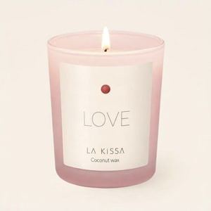 May include: A lit pink candle in a frosted glass jar. The label reads "LOVE" with "LA KISSA" and "Coconut wax" below. A small red dot is above the word "LOVE". The candle is a home decor item.