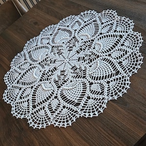 Può includere: Tovaglietta all'uncinetto bianca con un delicato motivo floreale. La tovaglietta è di forma ovale e presenta un design a pizzo.