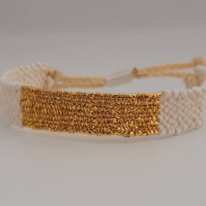 May include: A white and gold friendship bracelet with a woven design. The gold section is a textured band.