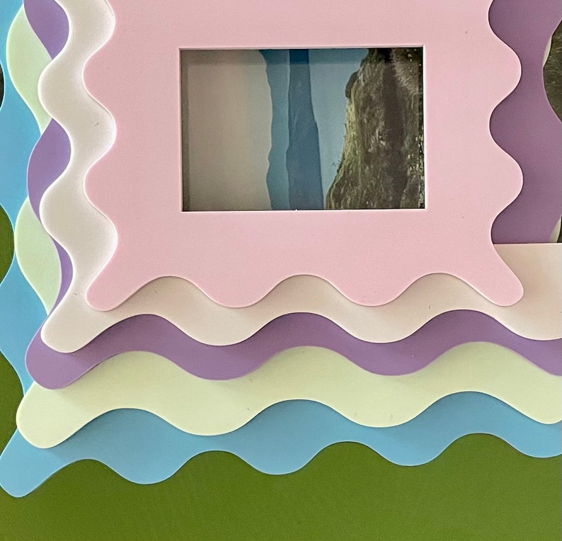 May include: A set of five colorful picture frames with wavy edges. The frames are layered on top of each other, with the largest frame on the bottom and the smallest frame on top. The frames are in shades of green, blue, light yellow, purple, and white.