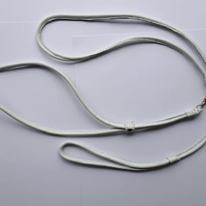May include: A white leather dog leash with a loop handle and a metal clasp. The leash is made of a smooth, flexible material and is designed for comfort and control. The leash is a simple, yet stylish accessory for dog owners.