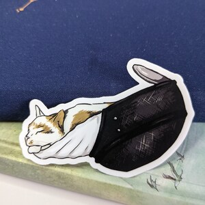 May include: A white, orange, and brown cat is curled up and sleeping inside a black and white helmet. The helmet has a white lining and a black strap.