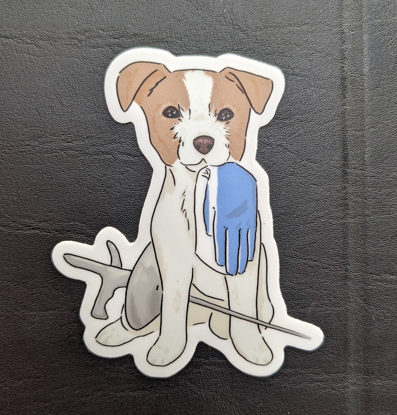 May include: A white and brown dog with blue eyes is holding a blue glove in its mouth. The dog is sitting on a white background with a grey and white stick behind it.