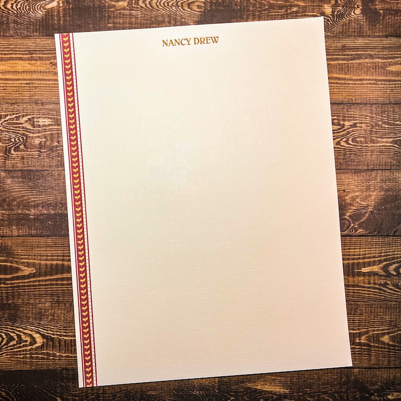 May include: A blank white sheet of paper with a red and gold border. The paper has the text "NANCY DREW" printed at the top.