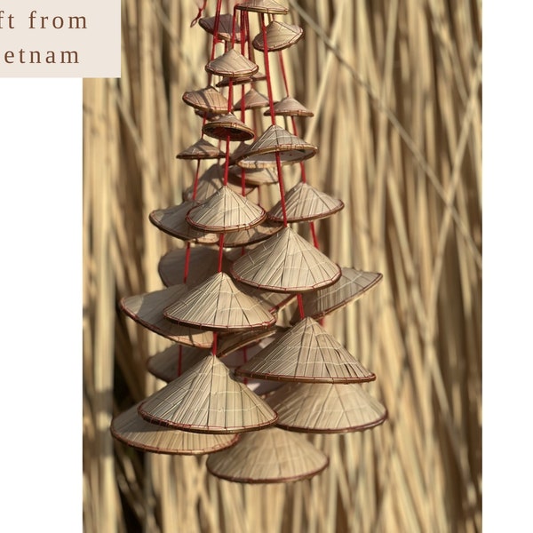 May include: A collection of small, woven conical hats hanging from red strings. The hats are made of natural-colored straw and are arranged in a cascading pattern. The text "Gift from Vietnam" is in the upper left corner.
