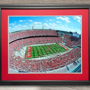 May include: An aerial view of a packed football stadium with a marching band forming the words "Ohio State" on the field. The stadium is filled with fans wearing red and white.