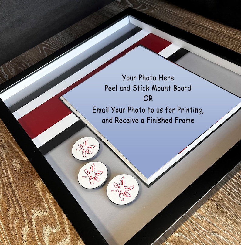 K&ouml;nnte beinhalten: Ein schwarzer Bilderrahmen mit einem wei&szlig;en, roten und grauen Passepartout. Der Rahmen hat einen blauen Hintergrund mit dem Text "Your Photo Here Peel and Stick Mount Board OR Email Your Photo to us for Printing, and Receive a Finished Frame". Drei rote Ahornblattaufkleber befinden sich auf dem Passepartout.
