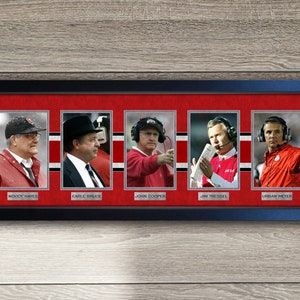 May include: Framed collage of five headshots of Ohio State University football coaches. The coaches are Woody Hayes, Earle Bruce, John Cooper, Jim Tressel, and Urban Meyer. Each coach is wearing a red and gray uniform and a headset. The background is red with white stripes.