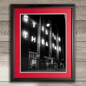 May include: Black and white photograph of a theater marquee with the words "Stadium Theatre" in illuminated letters. A crowd of people stand in front of the theater entrance.