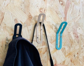 May include: Three metal hooks mounted on a wood panel wall. The hooks are in different colors: black, beige, and teal. A black jacket is hanging on the black hook.