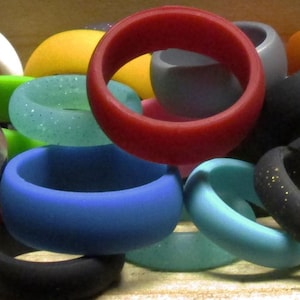 May include: A collection of colorful silicone rings in various shades of blue, green, red, orange, yellow, brown, black, and white. The rings are stacked and arranged in a random pattern.