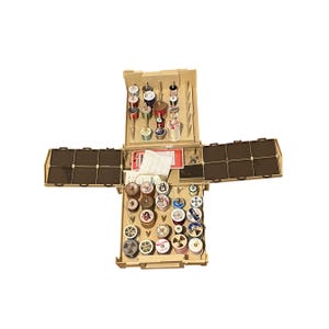 May include: Open beige sewing box filled with spools of thread in various colors. The box has multiple compartments and hinged side panels. A variety of thread colors are visible, including red, blue, white, and green. The box is open, displaying its contents.