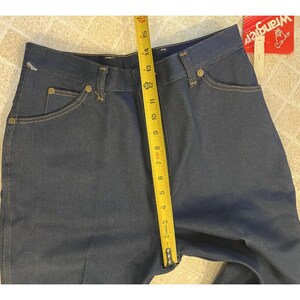 May include: Dark blue denim jeans with a yellow measuring tape showing a length of approximately 15 inches. The jeans have classic five-pocket styling and a Wrangler tag.