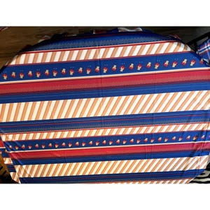 May include: A round tablecloth with a blue, red, and white striped pattern. The stripes are diagonal and have a geometric design.