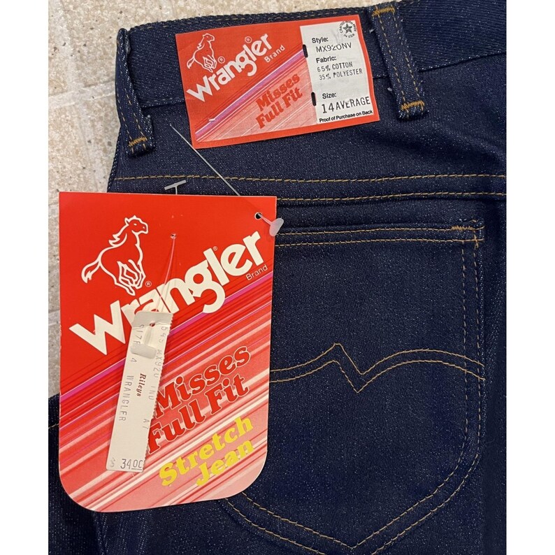 May include: Dark blue Wrangler Misses Full Fit stretch jeans with a red Wrangler brand tag. The tag displays a running horse logo and the text "Misses Full Fit Stretch Jean". The jeans are size 14 Average.