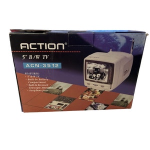 Op de afbeelding: Een wit-grijze 5-inch zwart-wittelevisie met een ingebouwde antenne, batterijvak en koptelefoonaansluiting. De doos heeft de tekst "ACTION" en "ACN-3512".