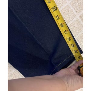 May include: Dark blue denim pants being measured with a yellow tape measure. The tape measure shows a length of approximately 23 to 31 inches. The pants have a classic five-pocket design.