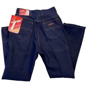 May include: Dark blue Wrangler jeans with a high waist and a classic fit. The jeans have a straight leg, a Wrangler label, and a tag that reads "Misses Full Fit". The back pockets have a distinctive curved design.