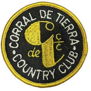 May include: Circular embroidered patch with the text "CORRAL DE TIERRA COUNTRY CLUB" in white, curving around a black circle. The centre features a gold-coloured stylized "9" and "c/t". The patch has a gold border.