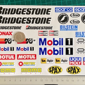 May include: A sheet of white stickers with various car racing brands and logos, including Bridgestone, Sparco, Aral, Bilstein, K&N, Mobil 1, Motul, Pirtek, Champion, OZ Racing, Agip, Liqui Moly, Momo, and Spax.