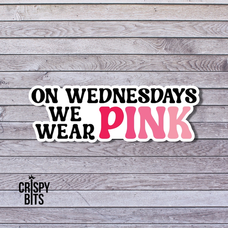 May include: A sticker with the text "On Wednesdays We Wear Pink" in black and pink lettering on a white background. The sticker is on a woodgrain background.