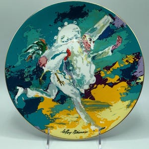 May include: Circular decorative plate with a gold rim, depicting a running figure in a white costume with a rooster, in an abstract style. The artist's signature, "LeRoy Neiman", is visible.