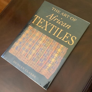 May include: A hardcover book titled "THE ART OF African TEXTILES" by Duncan Clarke. The book cover is dark green with gold lettering. The cover features a colorful textile pattern in shades of blue, yellow, and red.