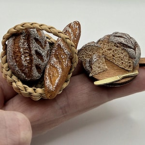 May include: Miniature bread set. A woven basket holds two loaves and a baguette. A sliced loaf sits on a wooden board with a small knife. The bread is light brown with white accents, giving a realistic, textured look.