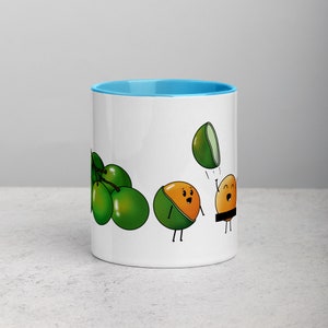 May include: White ceramic mug with a light blue rim. The mug features a cartoon illustration of green limes and a yellow lime with a face. The lime is throwing another lime in the air.