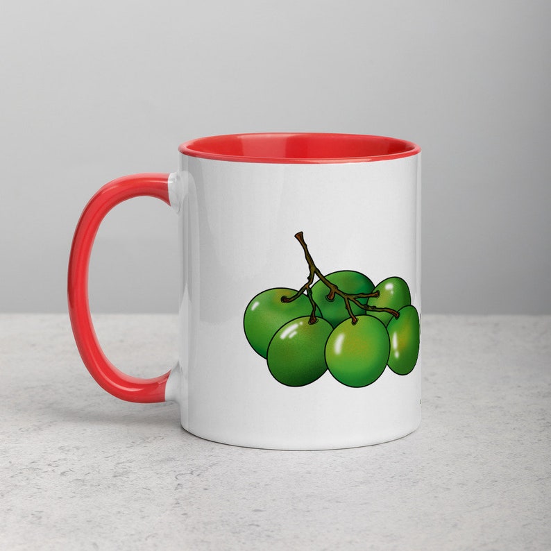 May include: White ceramic mug with a red rim and handle. The mug features a cartoon illustration of a bunch of green olives.