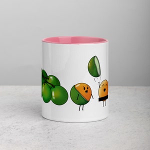 May include: White ceramic mug with a pink rim. The mug features a cartoon illustration of green limes and a lime with a face throwing another lime with a face. The lime with a face is wearing a brown belt.
