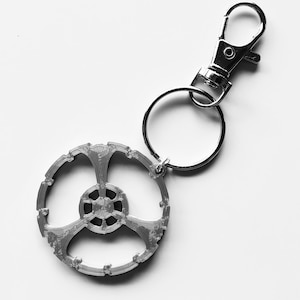 May include: A silver keychain with a circular, three-pronged design and a silver split ring attached to a silver lobster clasp.