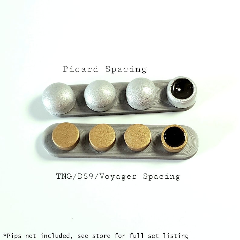 Puede incluir: Dos filas de piezas redondas de pl&aacute;stico de color plateado y dorado, con una pieza negra al final de cada fila. El texto "Picard Spacing" est&aacute; por encima de la fila superior y "TNG/DS9/Voyager Spacing" est&aacute; por debajo de la fila inferior. *Pips no incluidos, consulte la tienda para la lista completa*.