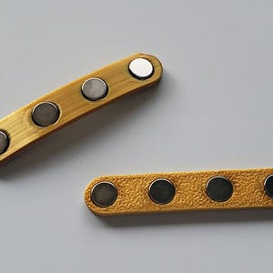 Puede incluir: Dos correas de cuero amarillo con cierres magn&eacute;ticos plateados. Las correas tienen cuatro y cinco cierres magn&eacute;ticos, respectivamente.