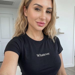 May include: Black crew neck t-shirt with the word "Whatever" printed in white. The shirt is worn by a person with blonde hair and blue jeans.