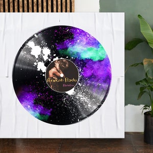 May include: A black vinyl record with a purple, blue, and green watercolour design. The record has a white label with the text "Erykah Badu" and "Baduizm" in black.